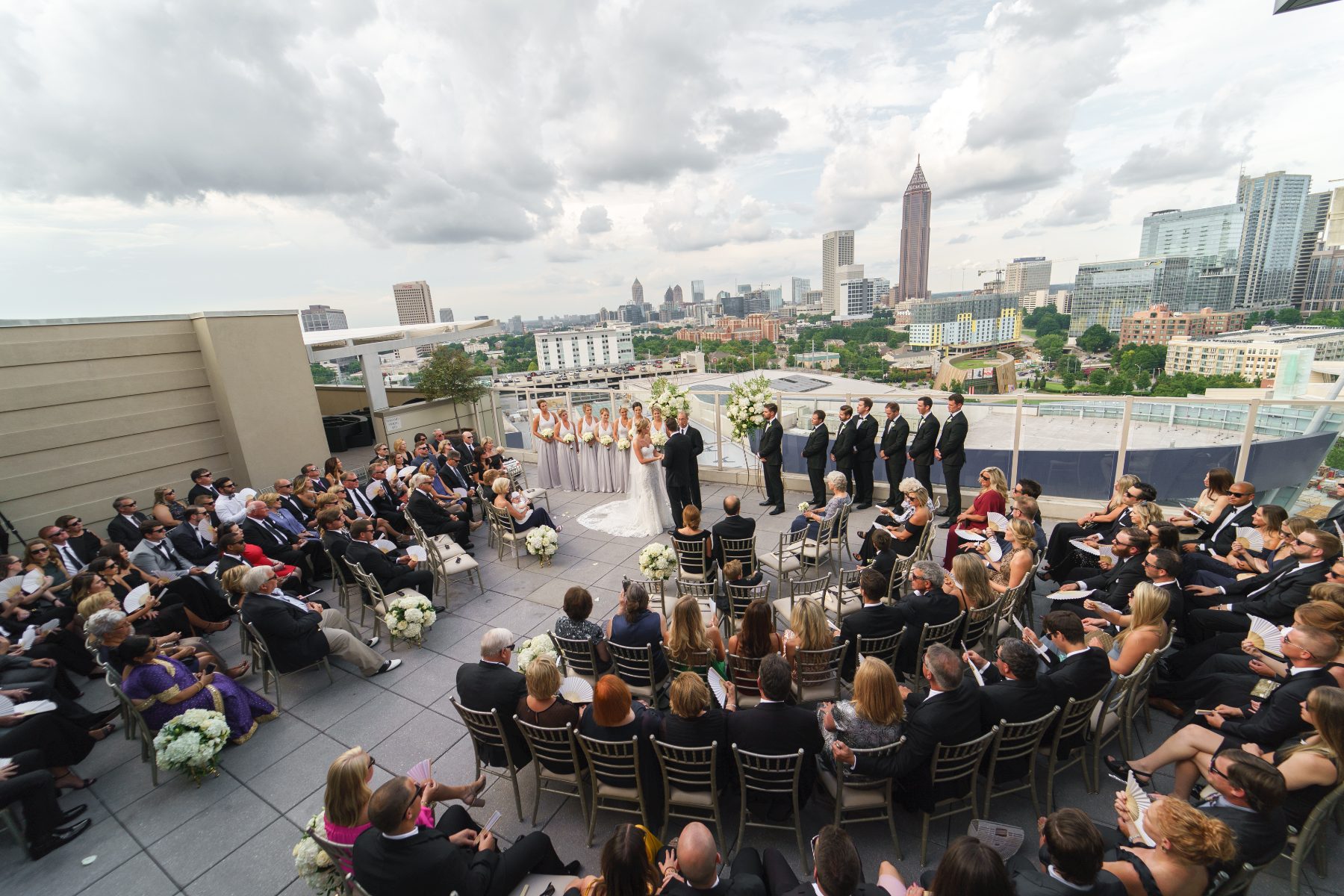 A couple exchanging vows at a rooftop ceremony in Midtown, with the Atlanta skyline and the Bank of America Plaza spire behind them