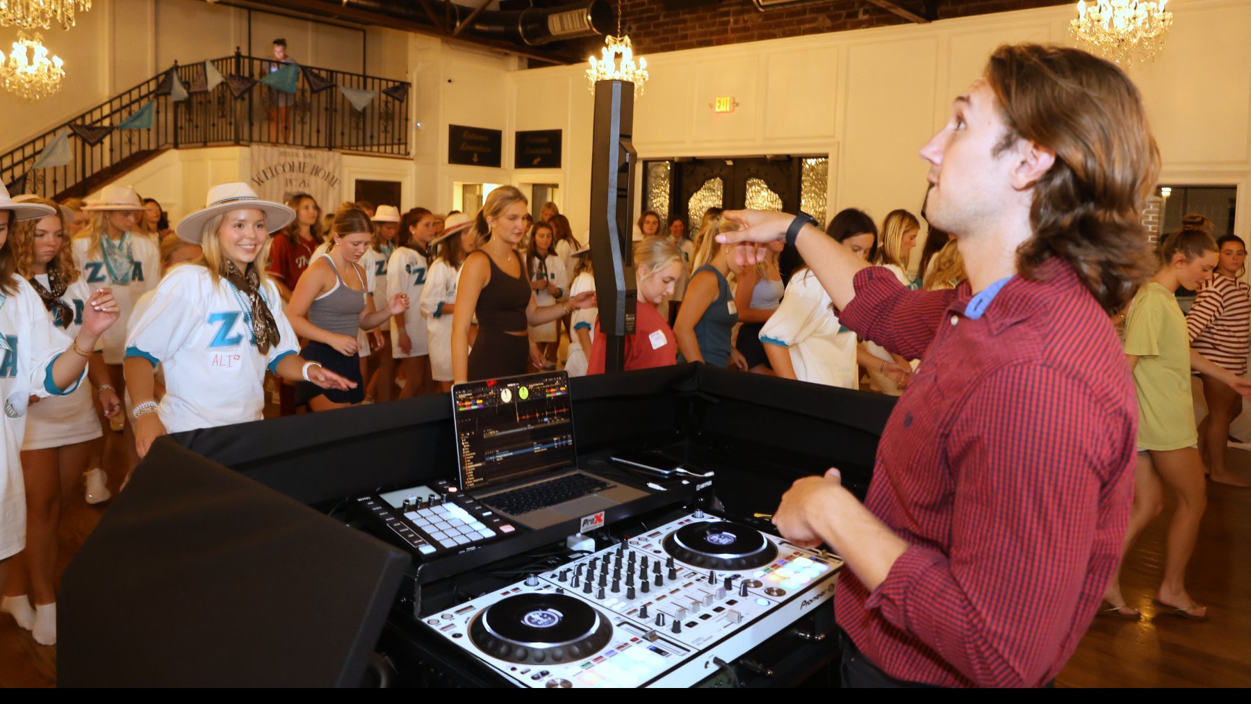A Nightbird DJ working the controller as a sorority chapter fills the floor of a historic hall under chandeliers, Athens, Georgia