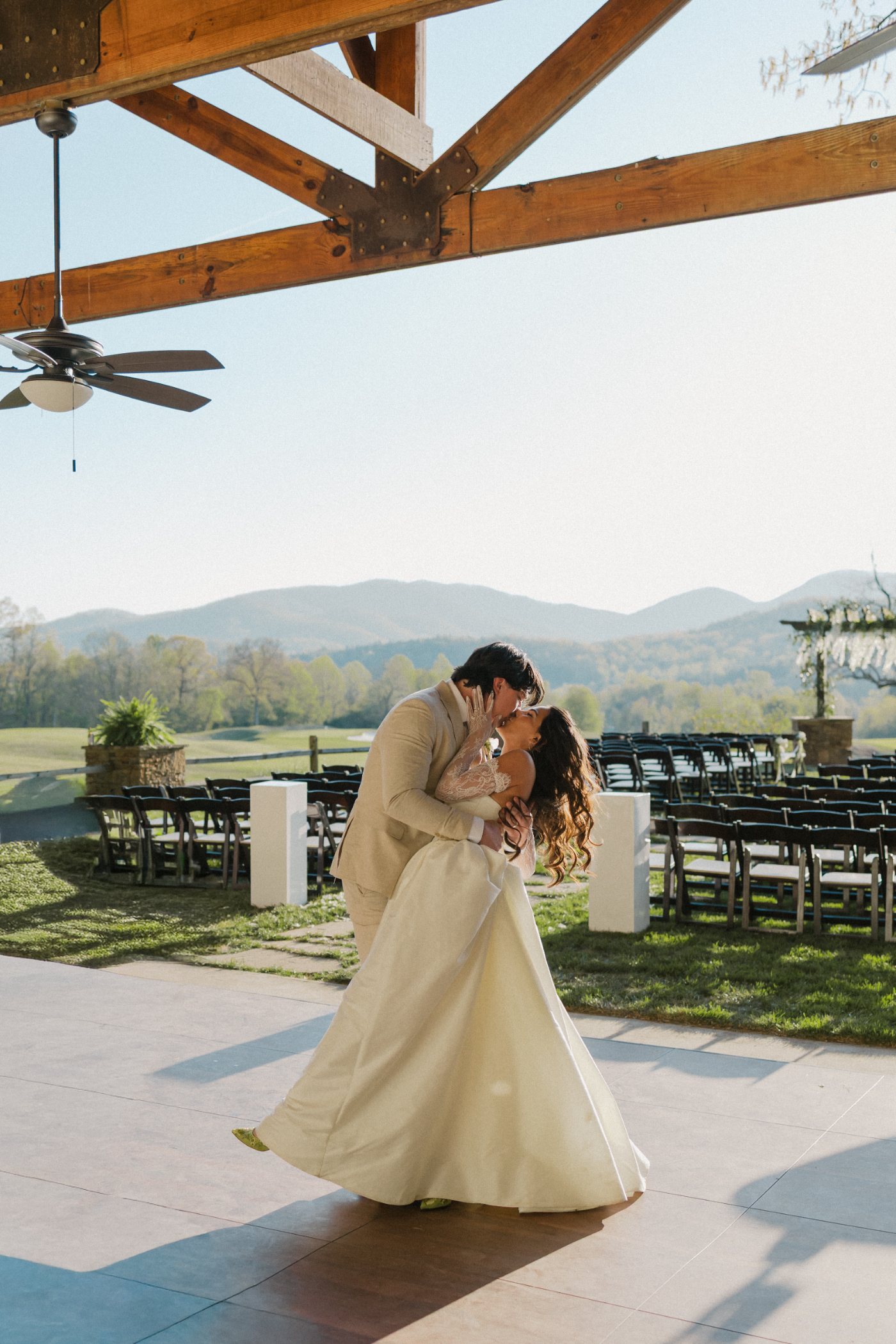 A couple dip-kissing on an open-air pavilion dance floor with the north Georgia mountains behind them