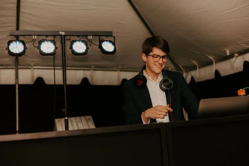 A Nightbird DJ smiling behind the booth under an event tent, four par cans on a stand alongside