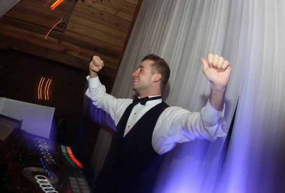 A Nightbird DJ in a bow tie, both arms up behind the decks