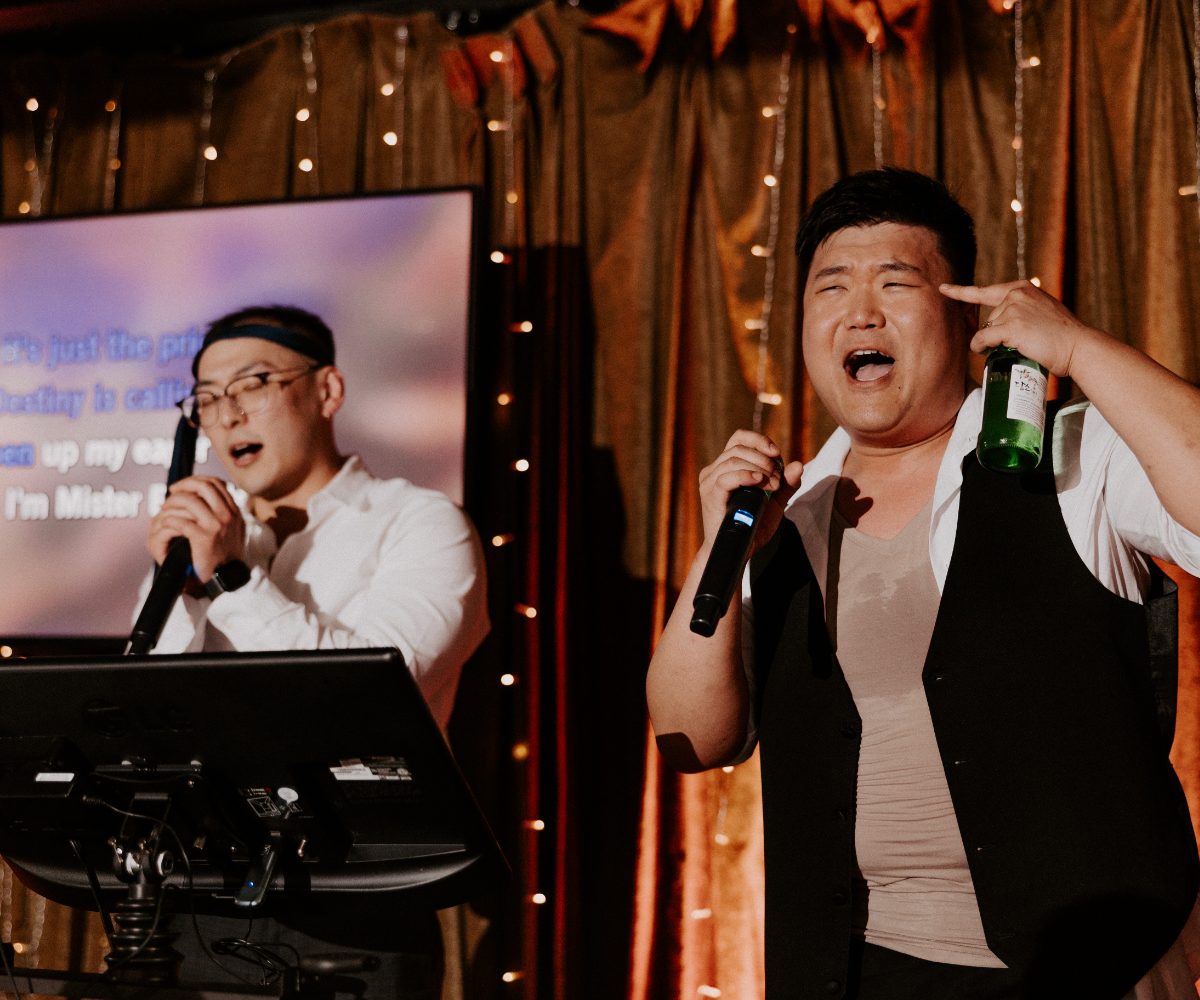 Two guests singing karaoke at a Nightbird party, lyrics on the screen behind them