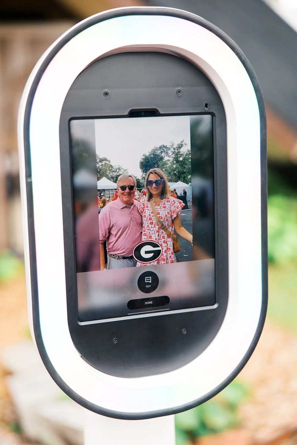 The Nightbird booth screen showing a couple with a custom G overlay at a UGA tailgate, tents behind